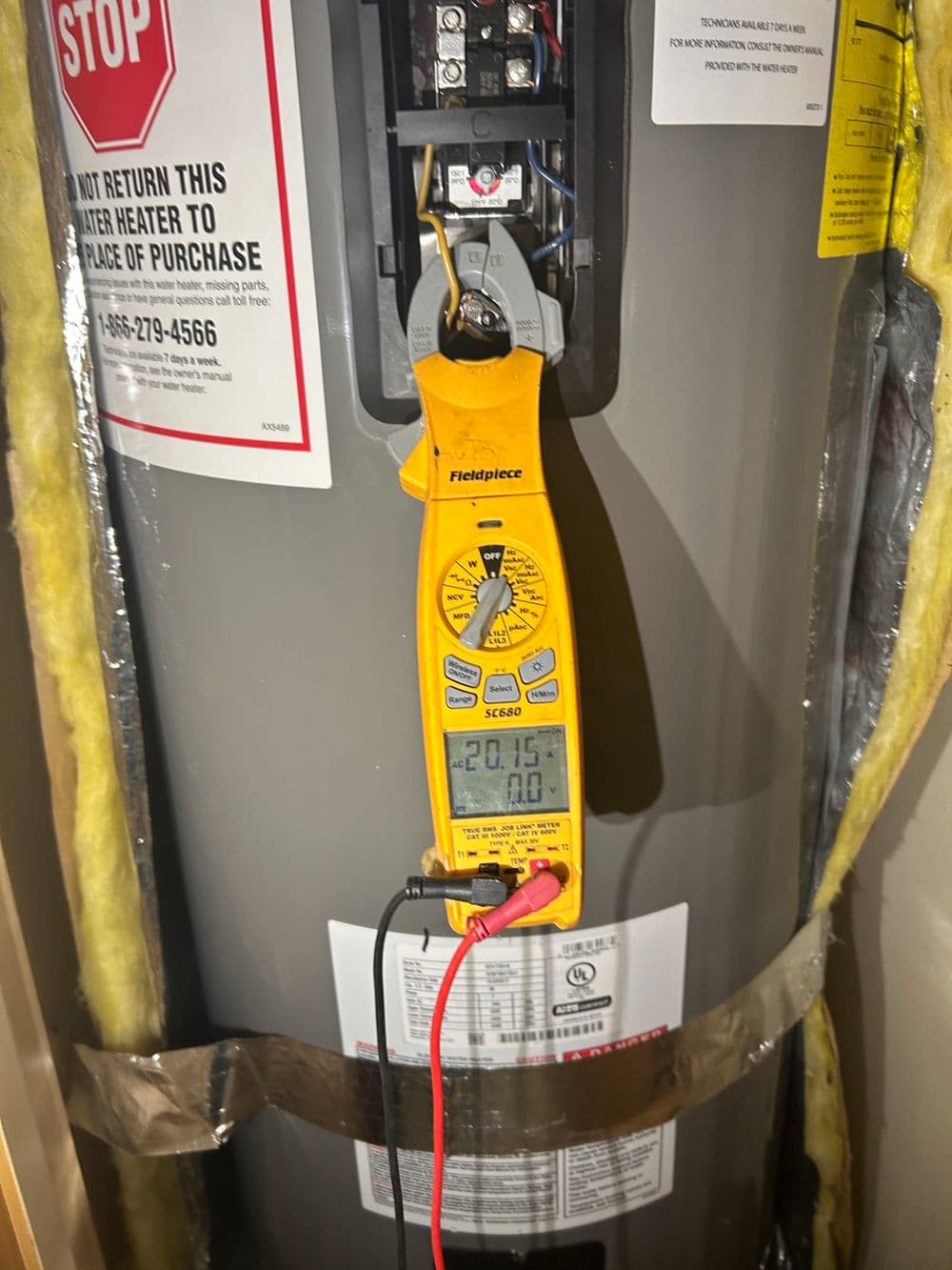 Electrical multimeter measuring voltage on a water heater in a utility room.