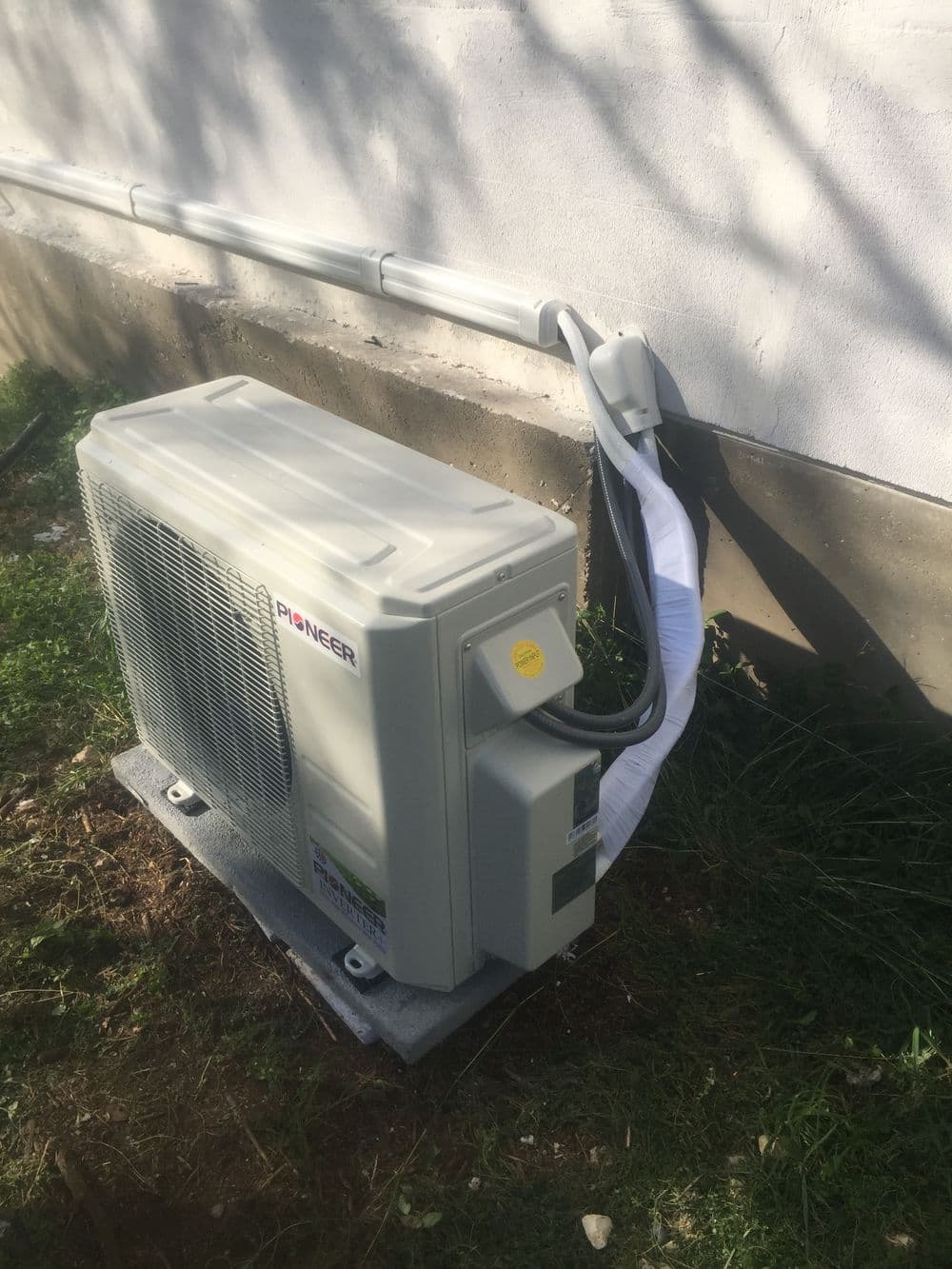 Pioneer air conditioning unit installed outside a building with drainage pipe and grass.